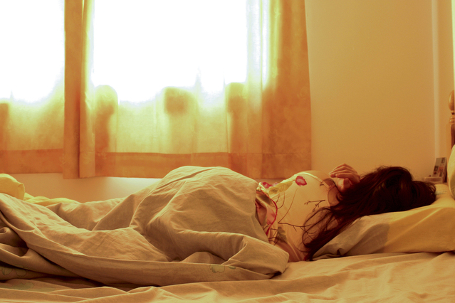Žena spí v posteli zakrytá paplónom